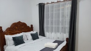 Una cama bien hecha con cabecera de madera, ropa de cama blanca y azul oscuro, y una manta gris.