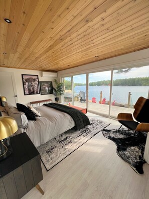 A bedroom with a large bed, a desk, a chair, and a view of a lake through large windows. - Muskoka Lakefront Resort - 5 Bedroom Modern Cottage (Muskoka Lakes)