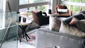 A modern living room with a wooden ceiling, large windows, a glass table, and comfortable seating. - Muskoka Lakefront Resort - 5 Bedroom Modern Cottage (Muskoka Lakes)