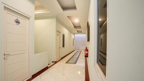 Un pasillo con suelo de baldosas blancas, un extintor de incendios montado en la pared y una puerta con el símbolo de número.