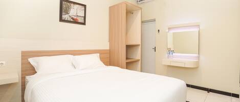 A hotel room with a bed, a wooden wardrobe, a wall-mounted air conditioning unit, a framed picture, and a mirror with a sink.