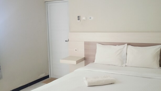 Una habitación de hotel con una cama, una mesita de noche, un panel de control en la pared y una puerta.