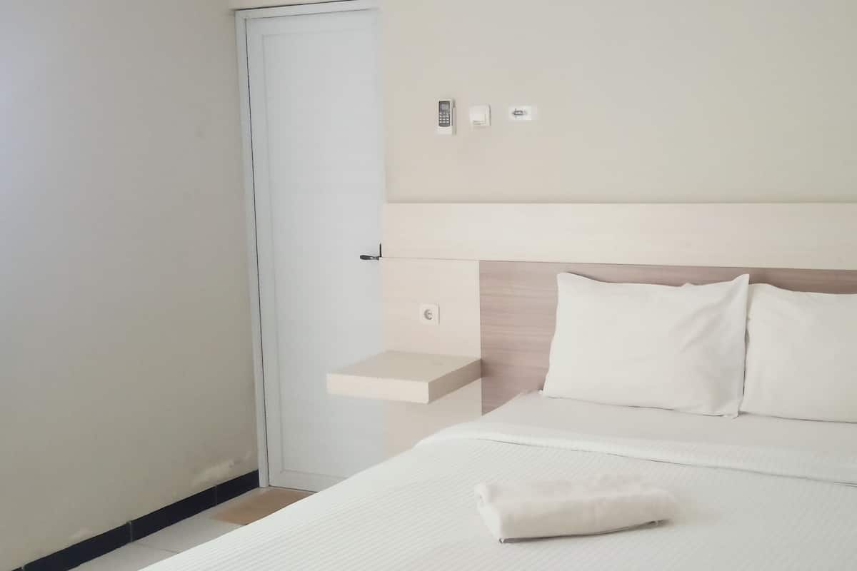 Una habitación de hotel con una cama, una mesita de noche, un panel de control en la pared y una puerta.