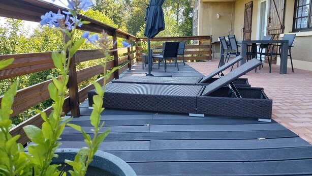 Un terrazzo in legno con mobili da esterno, tra cui un tavolo e sedie, e una poltrona in vimini.