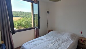 Un dormitorio con una cama, una ventana con cortinas, una lámpara de noche y una mesita de noche de madera.