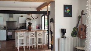 Una cocina con barra de madera, sillas blancas y una guitarra.