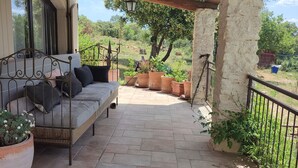 Un área de estar al aire libre techada con un sofá de mimbre, plantas en macetas y una pared de piedra.