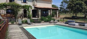 A poolside area with a wooden deck, lounge chairs, and a stone building with a tiled roof. - air-conditioned house in the countryside with swimming pool (Mirabeau)