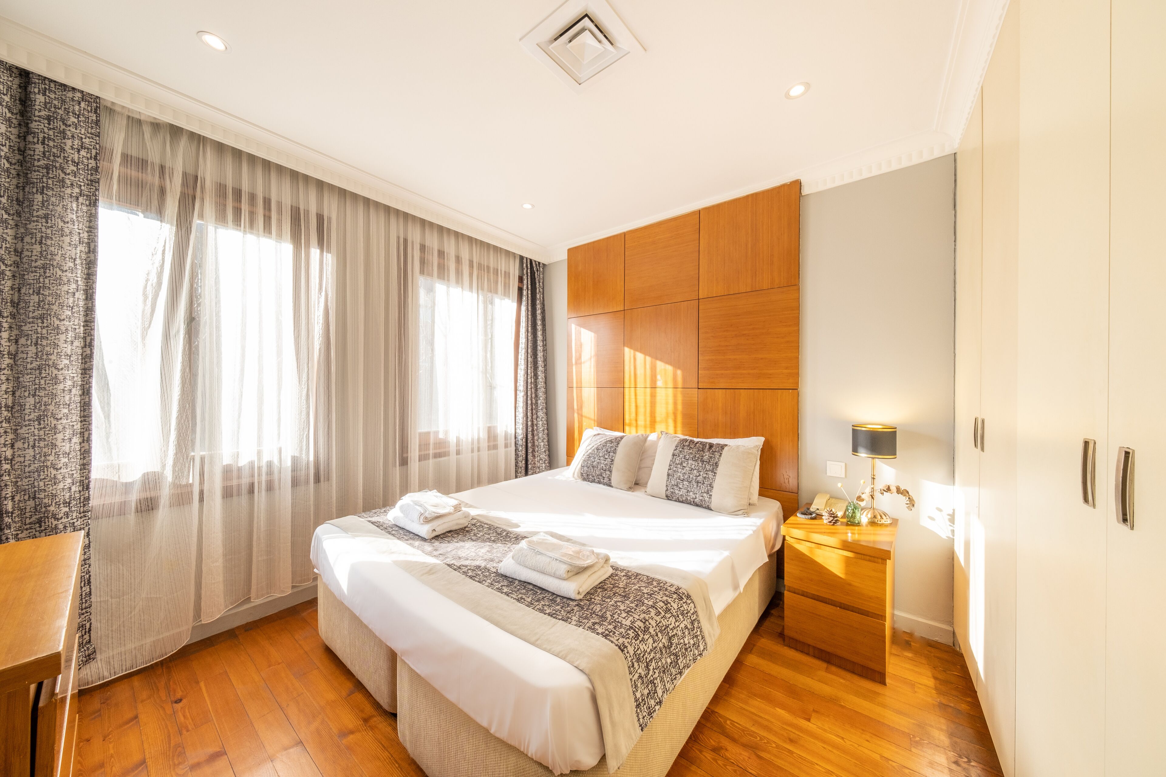 A hotel room with a large bed, wooden flooring, a desk, and a wardrobe.