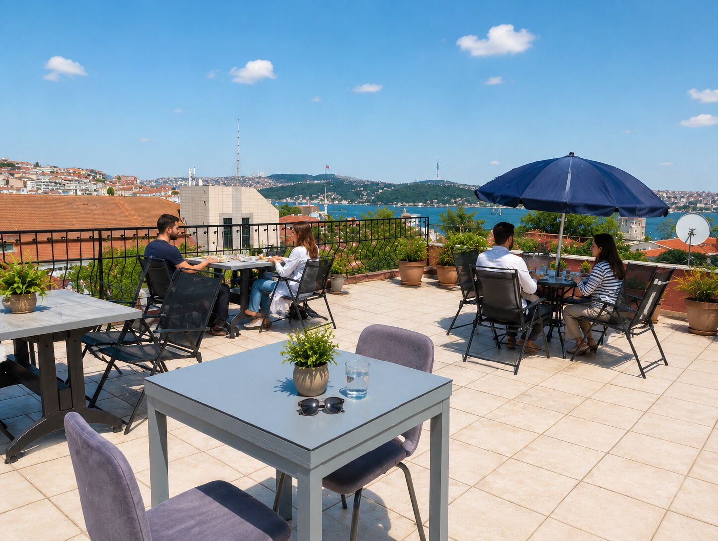 Una terraza con mesas y sillas, plantas en macetas y vistas a un pueblo costero.