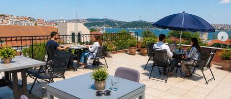 Una terraza con mesas y sillas, plantas en macetas y vistas a un pueblo costero.