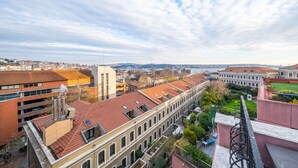 A multi-story building with a red-tiled roof, a courtyard with greenery, and a view of the cityscape in the background. - King Suits Hotel (Istanbul)