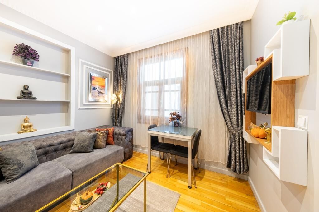 En moderne stue med en grå sofa, et glasbord, et spisebord og et tv-reol.