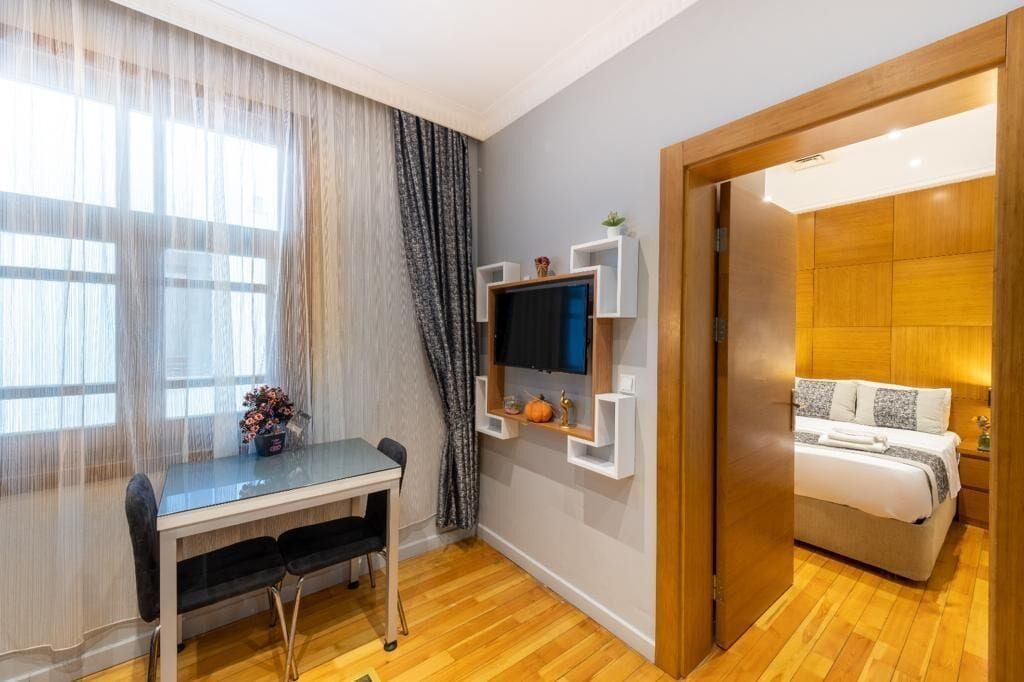 Een hotelkamer met een bed, een bureau met stoel, een aan de muur bevestigde televisie en een houten deur.