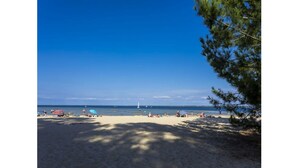 Ein Strand mit blauem Himmel, sandigem Ufer und ein paar Personen und Booten in der Ferne.