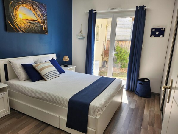 A bedroom with a bed, nightstands, a lamp, and a view of the outside.