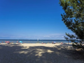 Ein Strand mit blauem Himmel, sandigem Ufer und ein paar Personen und Booten in der Ferne.