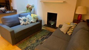 A modern living room with a grey sofa, a small table with a vase of flowers, a fireplace, and a red lamp.