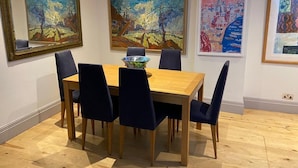 A dining area with a wooden table and dark blue chairs, surrounded by three framed paintings on the walls.