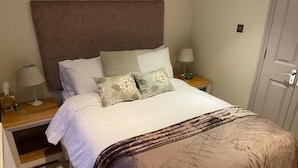 A neatly made bed with a brown headboard, two bedside tables with lamps, and a door to the right.