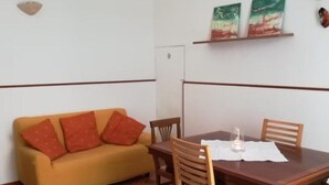Un comedor con una mesa y sillas de madera, un sofá con cojines naranjas y un piso de baldosas.