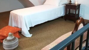 Un dormitorio con una cama individual, una mesita de noche con lámpara, una pequeña mesa con un jarrón y una silla.