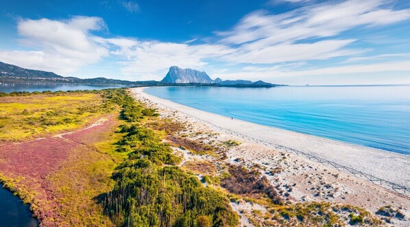 A coastal landscape with a beach, a mountain, and a clear sky.