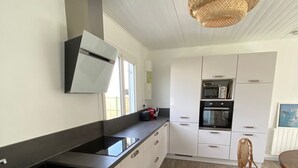 A modern kitchen with white cabinets, a black countertop, and a wicker pendant light. - The Saint Vaast orchard  (Saint-Vaast-la-Hougue)