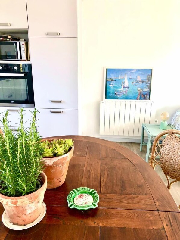 Une cuisine avec des meubles blancs, un four à micro-ondes et un tableau représentant un paysage côtier.