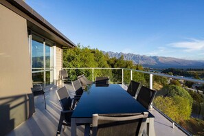 A modern outdoor dining area with a glass table and chairs, overlooking a mountainous landscape. - Alpen View Villa | Short walk to town (Queenstown)