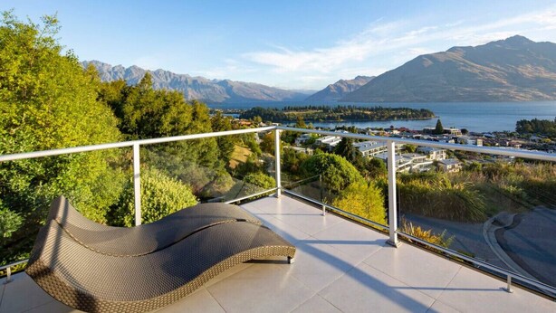 A balcony with a cushioned seating area overlooking a lake and mountains. - Alpen View Villa | Short walk to town (Queenstown)