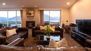 A modern living room with leather sofas, a coffee table, a flat-screen TV, and a fireplace. - Alpen View Villa | Short walk to town (Queenstown)