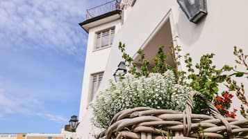 Ein Gebäude mit weißer Fassade, einem Balkon mit Metallgeländer und einem Korbwagen, gefüllt mit Blumen.