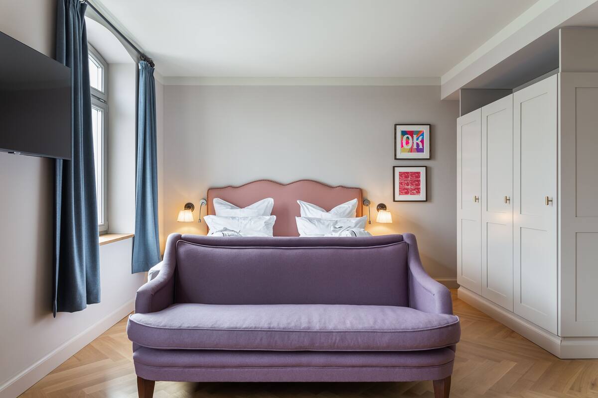 A modern bedroom with a large bed, a sofa, a TV, and a wardrobe.