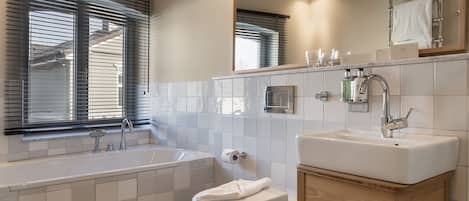 A modern bathroom with a bathtub, toilet, sink, and large mirror.