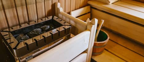 Una sauna con bancos de madera, un calentador de piedra y un cubo de madera.