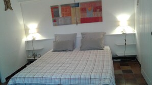 A bedroom with a bed, two bedside tables, two wall-mounted lamps, a clock, and a painting on the wall. - Appartement au Calme Dans un Parc Ombragé (Montignac)