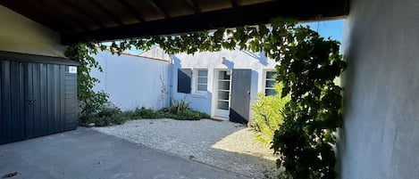 A covered outdoor area with a gravel path, a grey gate, and a building with a white facade and a window with a shutter.