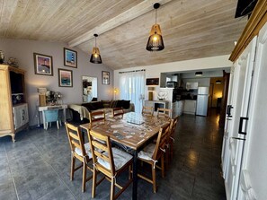 Een ruime eethoek met een houten tafel en stoelen, een keuken op de achtergrond, en een plafond met zichtbare houten balken.