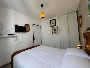 Un dormitorio con cama, televisor montado en la pared, una puerta y una mesita de noche con lámpara.