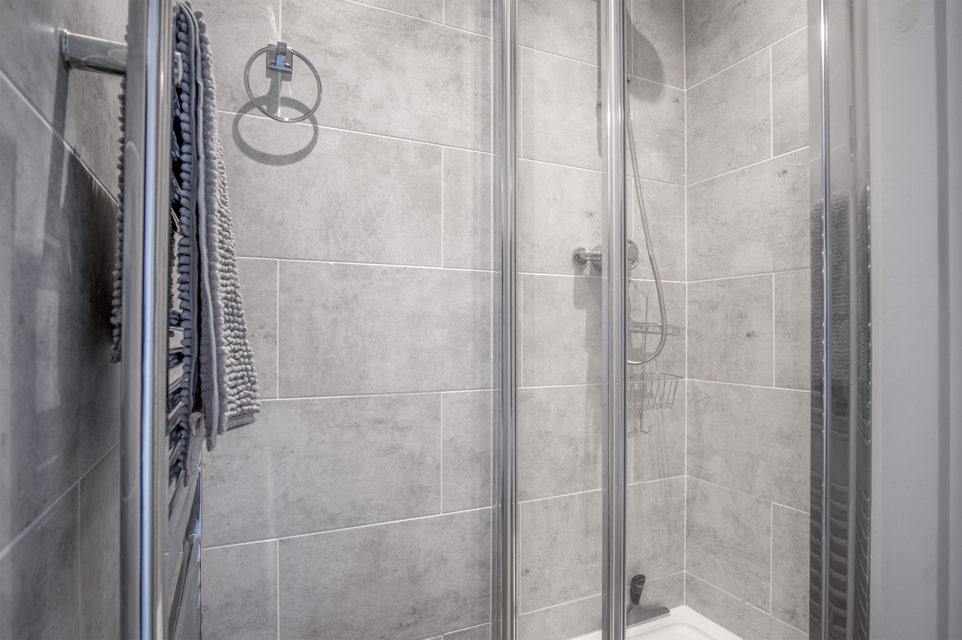 A glass-enclosed shower with grey tiles and a towel rack.