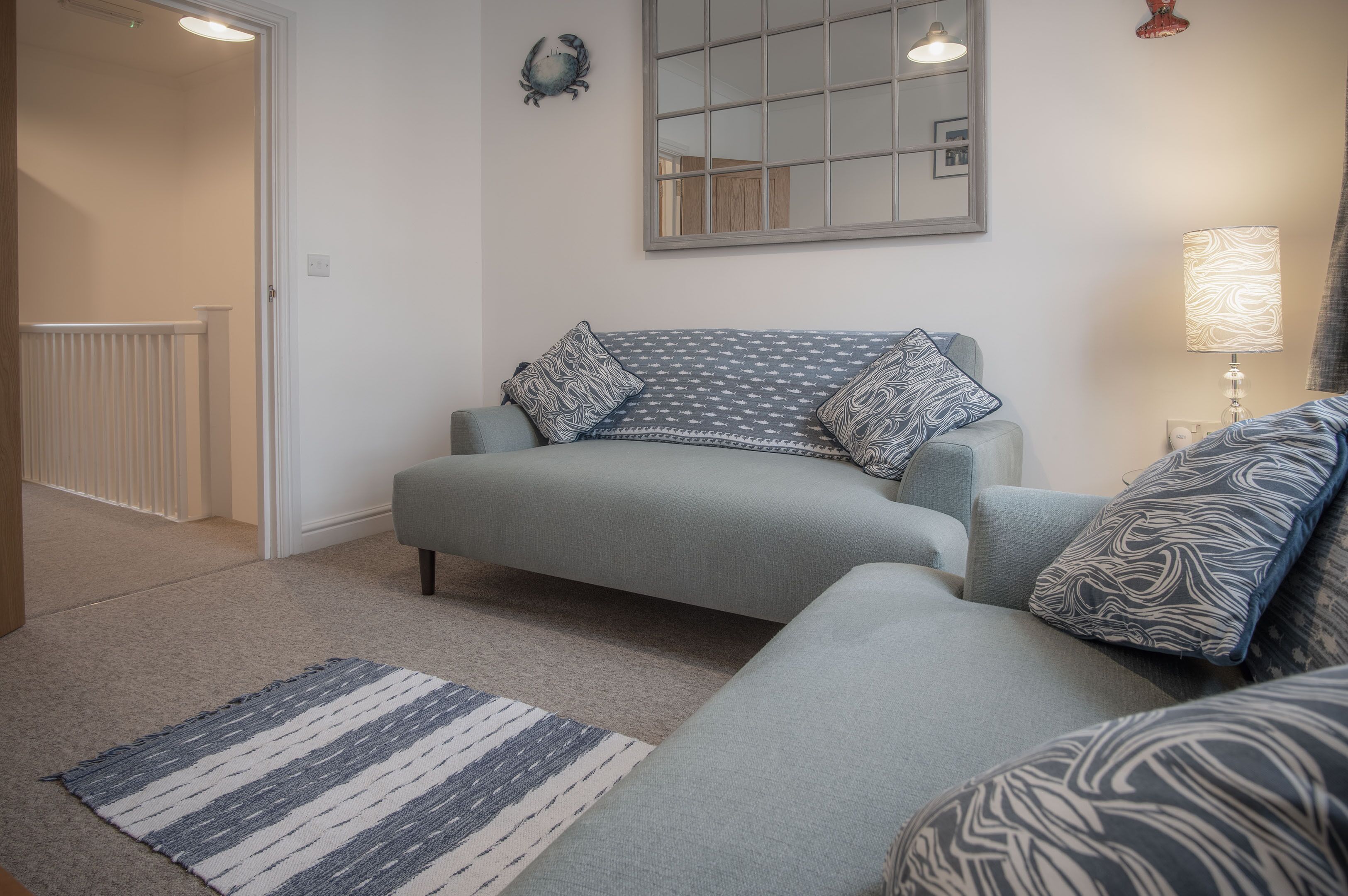 Un salon avec un canapé gris, des coussins à motifs, un tapis rayé, un miroir et une lampe.