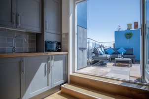 Una cocina moderna con armarios grises, un microondas y un lavamanos. Al exterior, hay un balcón con un sofá y una mesa, y una pared azul decorada con un corazón.