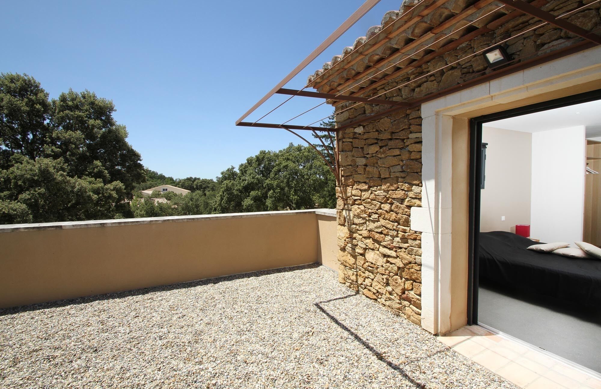 Varanda com parede de pedra, uma cama e vista para árvores e edifícios.