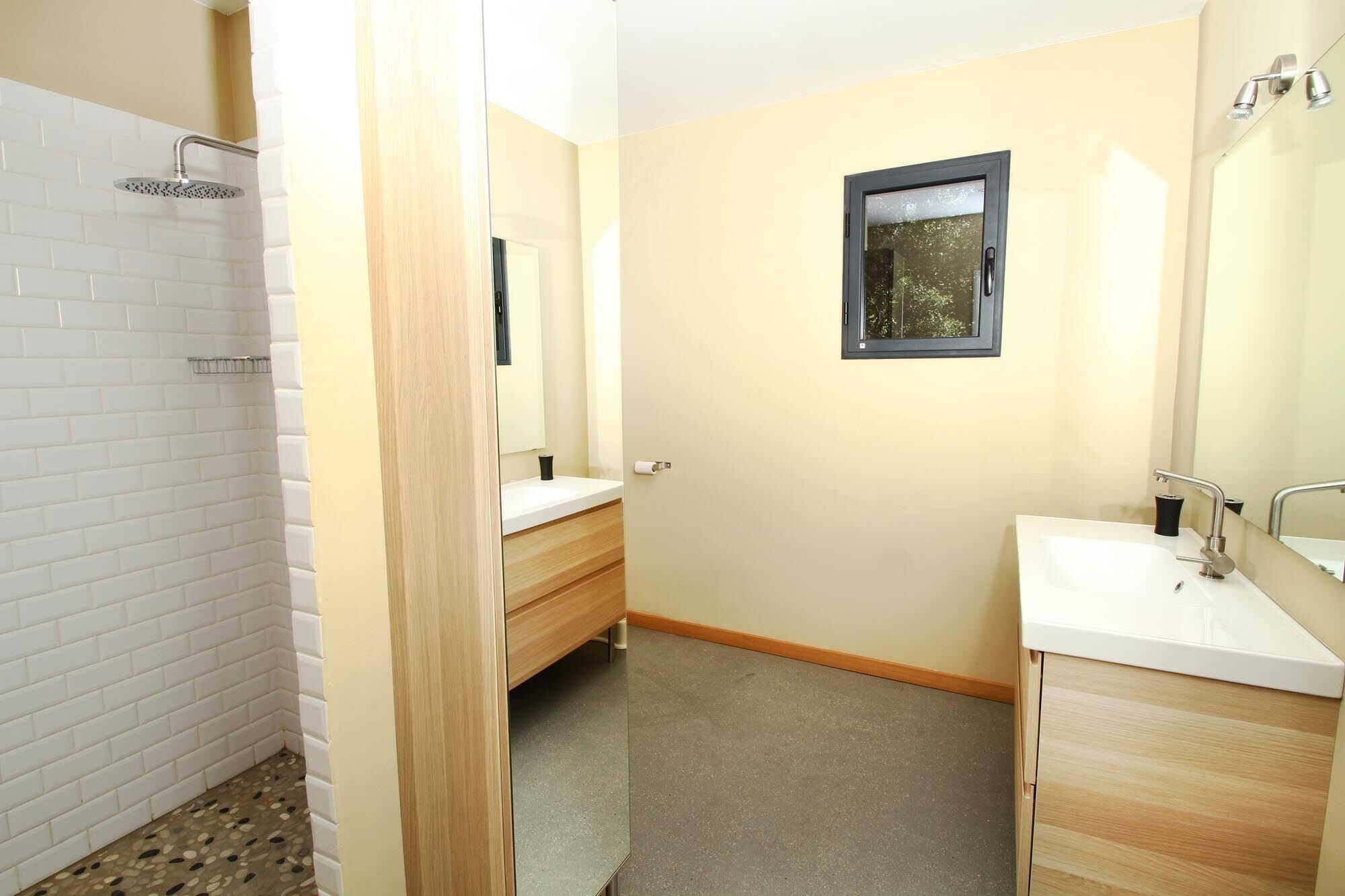Une salle de bain avec une douche, deux lavabos, un miroir et une petite fenêtre.