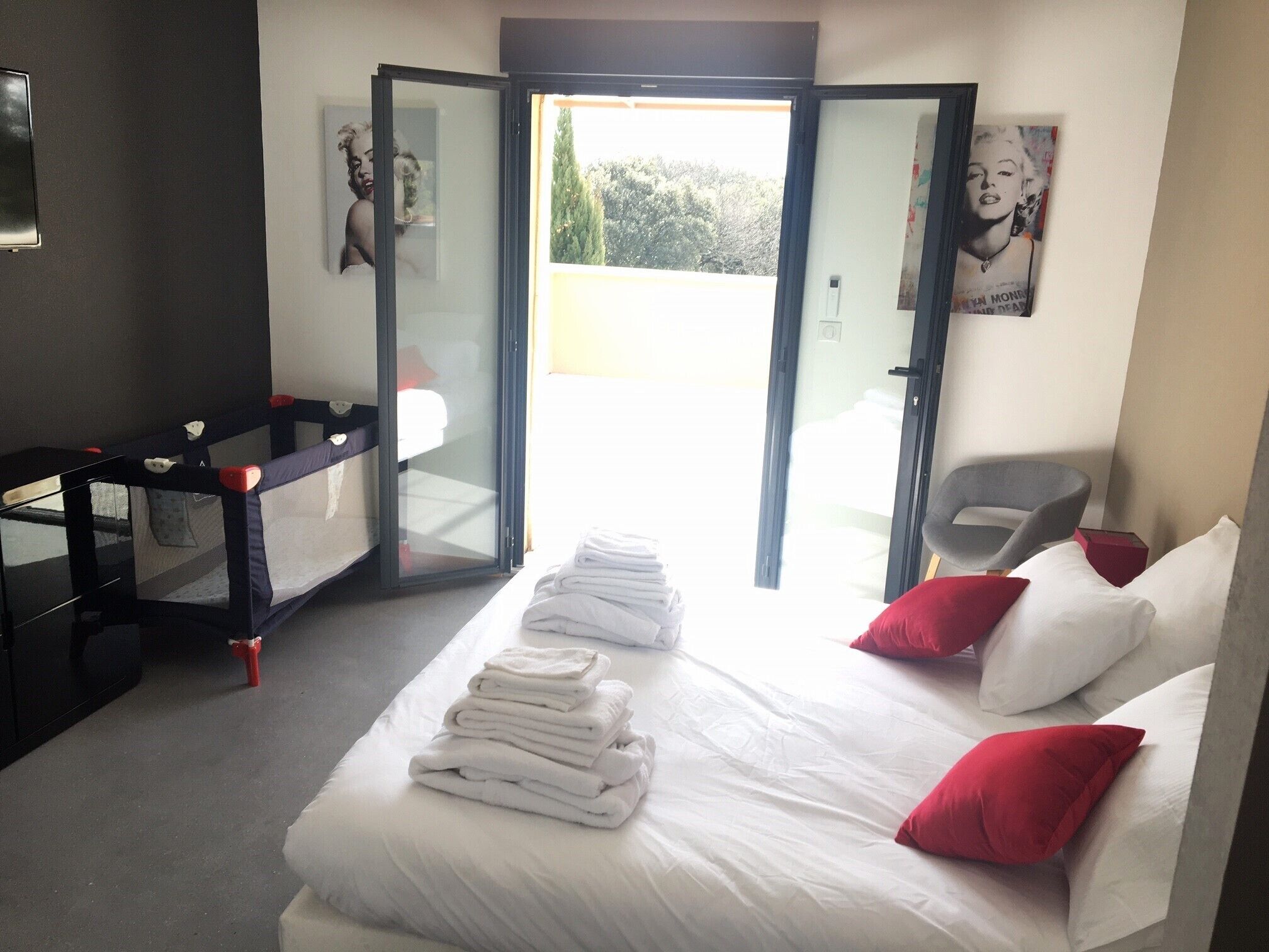 Habitación de hotel con cama, una silla, una mesita y un ventanal corredero que da a un espacio al aire libre.