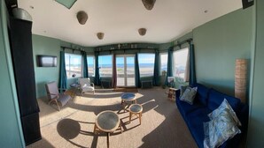 Ein Zimmer mit einem großen Fenster, einem blauen Sofa, einem runden Tisch und einem Sessel.
