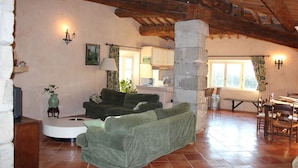 A cozy living room with a green sofa, a dining table with chairs, and a kitchen area in the background. - La Grange Domaine de la Blaque (Varages)
