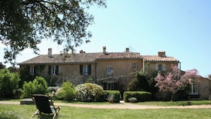 A large, two-story stone building with a tiled roof, surrounded by well-maintained lawns and various shrubs. - La Grange Domaine de la Blaque (Varages)