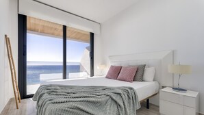 Une chambre à coucher moderne avec un grand lit, une table de chevet, une lampe et une vue sur l’océan.